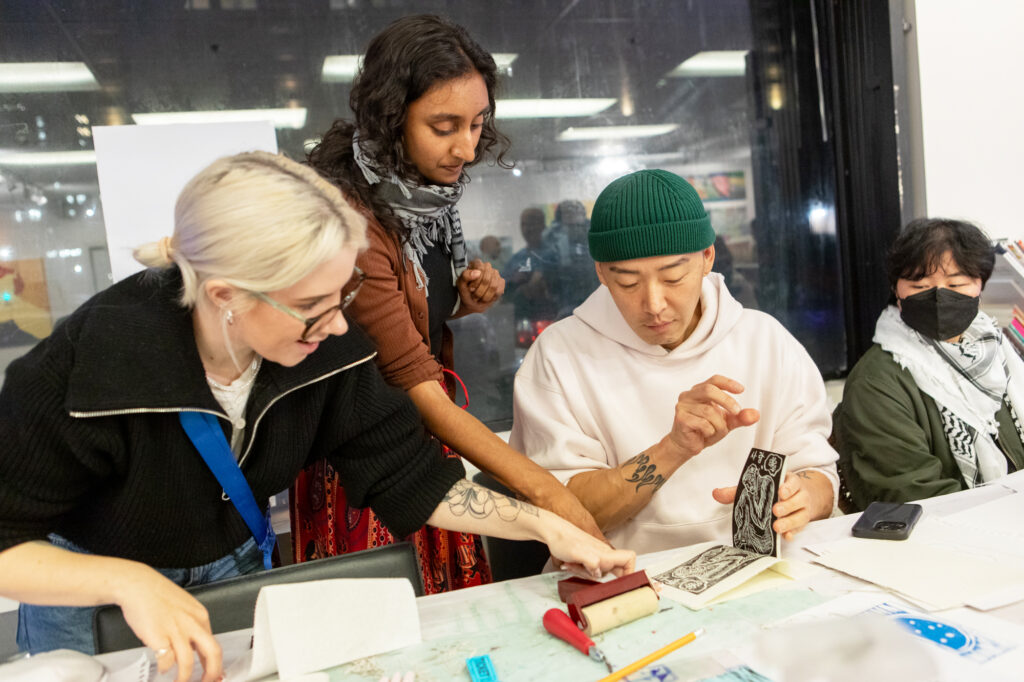 A group of people participating in a hands-on printmaking workshop with art tools on table.