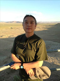 Artist Hung Liu standing in front of a green plain with mountains in the distance